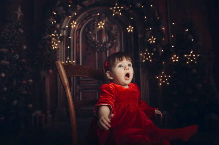Bambina con vestito di velluto rosso seduta su una sedia di legno, sfondo natalizio con luci dorate