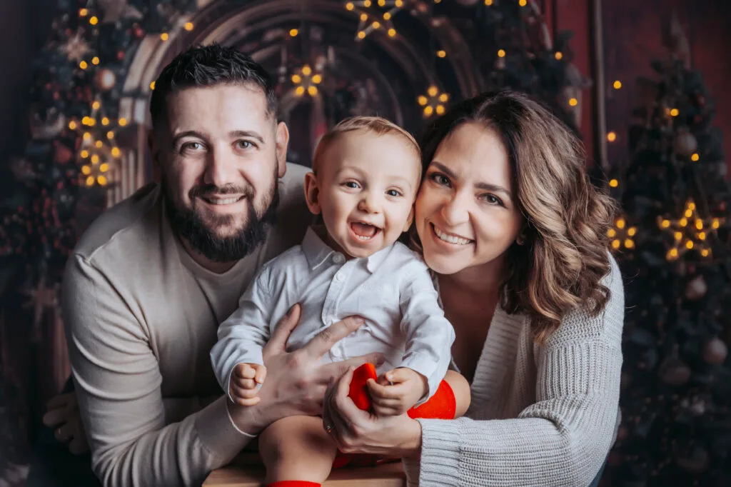Mamma e papà sorridenti con il loro bambino in braccio davanti ad alberi di Natale illuminati