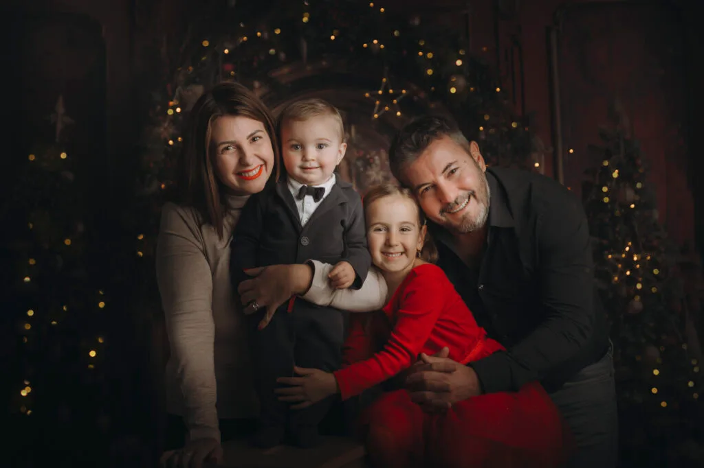 Famiglia di quattro persone abbracciata nel set di Natale con luci dorate, servizio fotografico di Natale a Roma